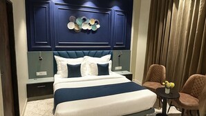 Une chambre d’hôtel moderne dotée d’un grand lit, d’un ventilateur de plafond, d’un panneau décoratif mural, d’un coin salon avec des fauteuils et d’un tapis à motifs de marbre.