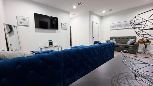 A modern living room with a blue sofa, a grey couch, and a TV mounted on the wall. - Beautiful 3BR Home • Stylish, Cozy & Convenient (Houston)