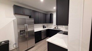 A modern kitchen with dark cabinets, a stainless steel refrigerator, and a white countertop. - Beautiful 3BR Home • Stylish, Cozy & Convenient (Houston)