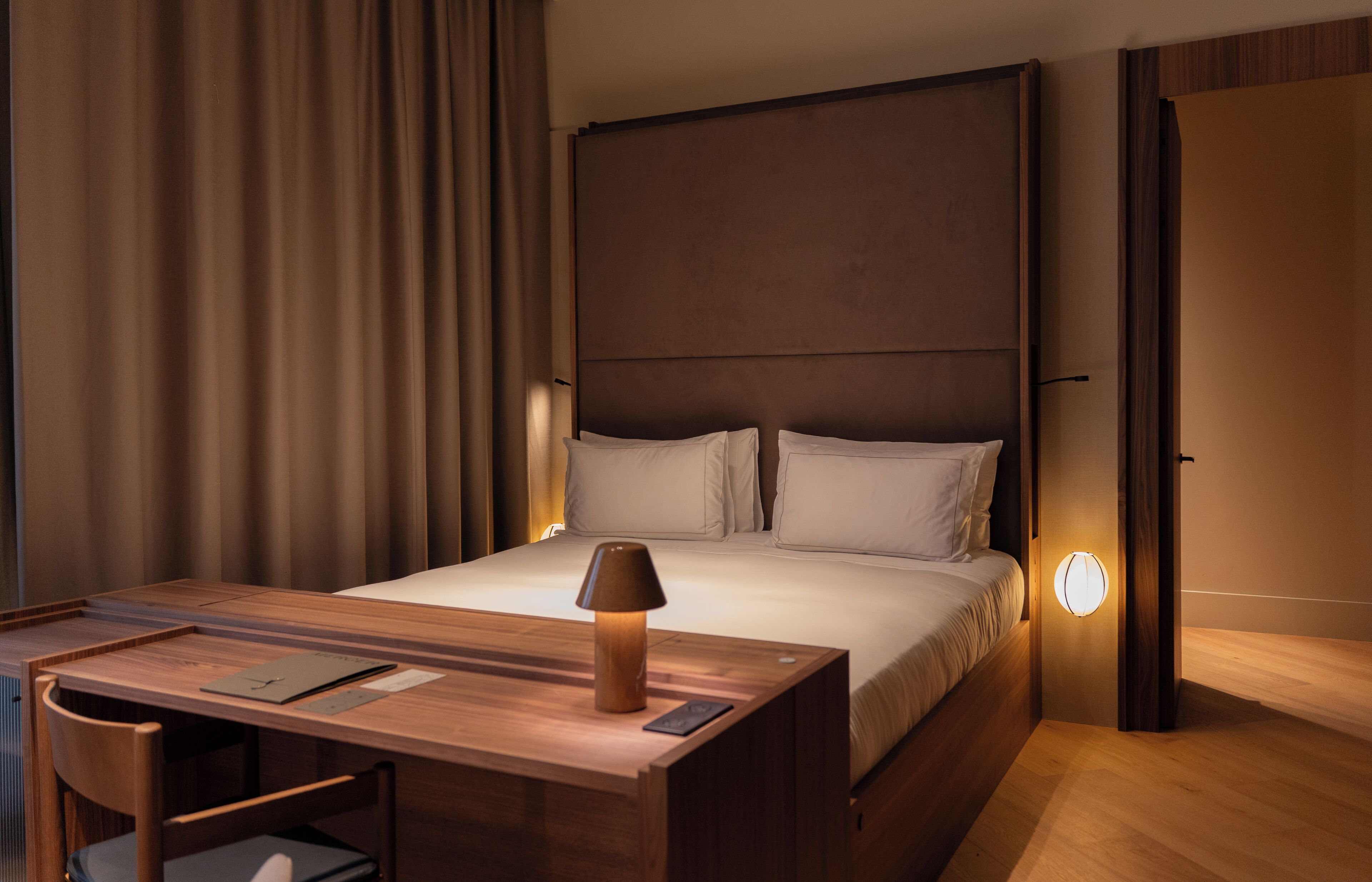 Una habitación de hotel con cama, mesita de noche, lámpara y escritorio con silla.