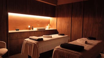 Une salle de spa équipée d’une table de massage, d’un petit lavabo et d’un miroir.