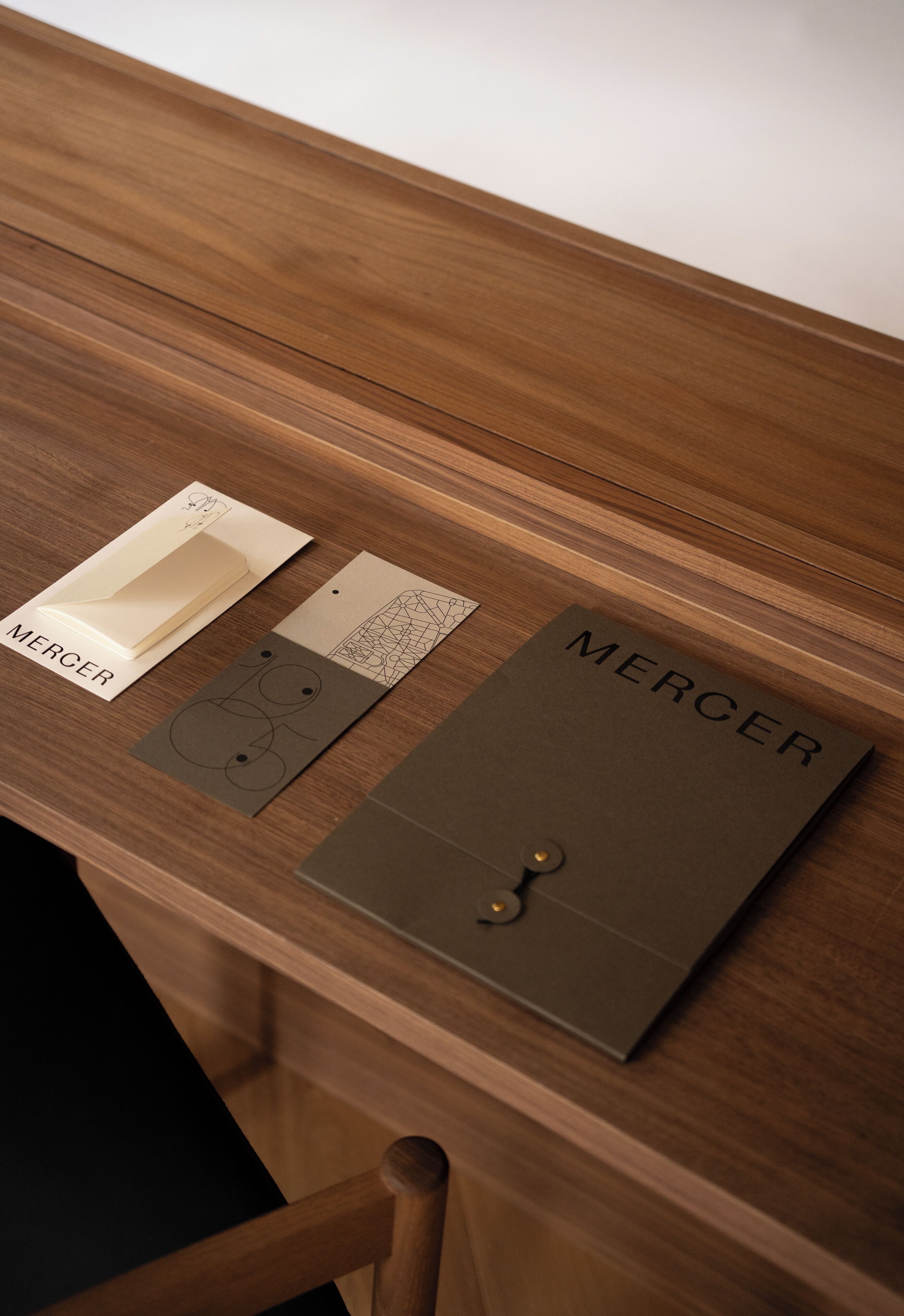 Ein Holztisch mit einer braunen Ordner, beschriftet 'MERCER', und zwei Karten mit Designs.