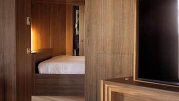 A modern hotel room with a wooden floor, a bed, a television, and built-in wooden cabinets.
