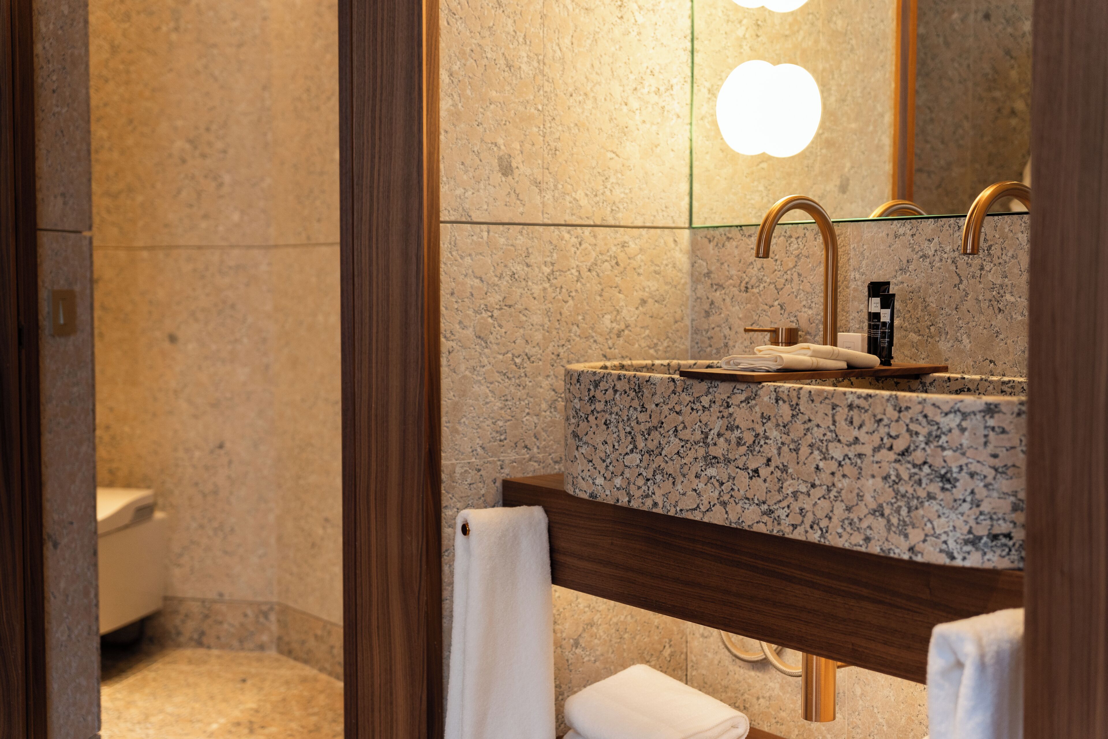 Un baño con encimera de granito, tocador de madera, espejo y retrete.