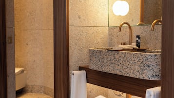 Un baño con encimera de granito, tocador de madera, espejo y retrete.