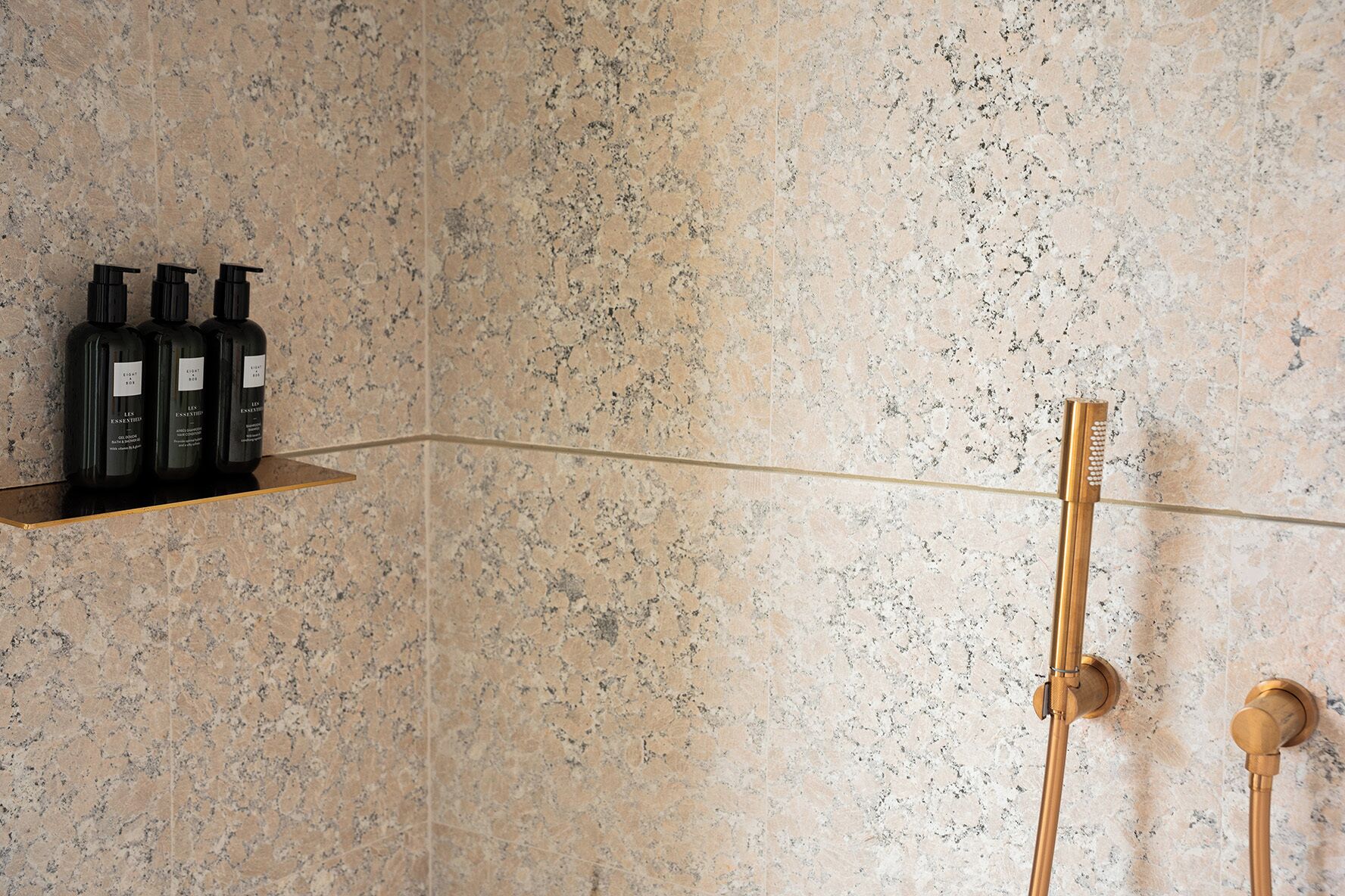 Ein Badezimmer mit Dusche, Ablagefläche mit Flaschen und Marmorwand.