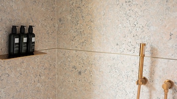 Ein Badezimmer mit Dusche, Ablagefläche mit Flaschen und Marmorwand.