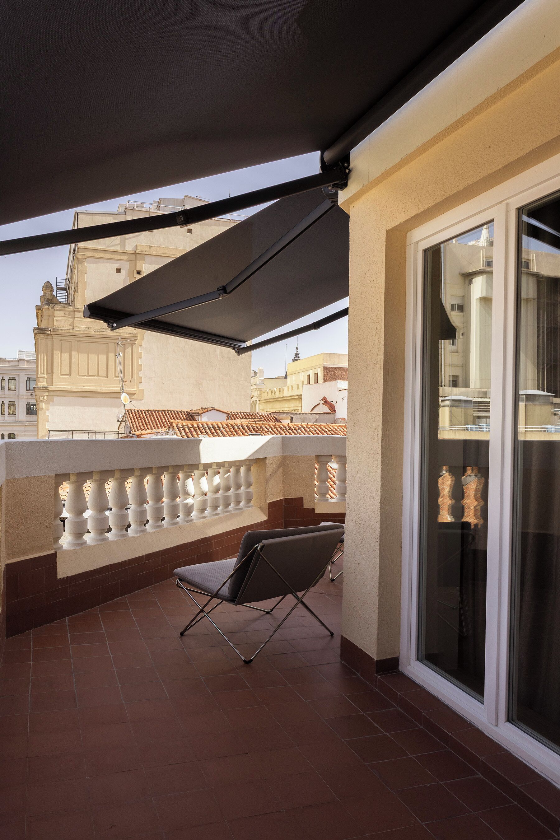 A balcony with a chair, a glass door, and a view of buildings.