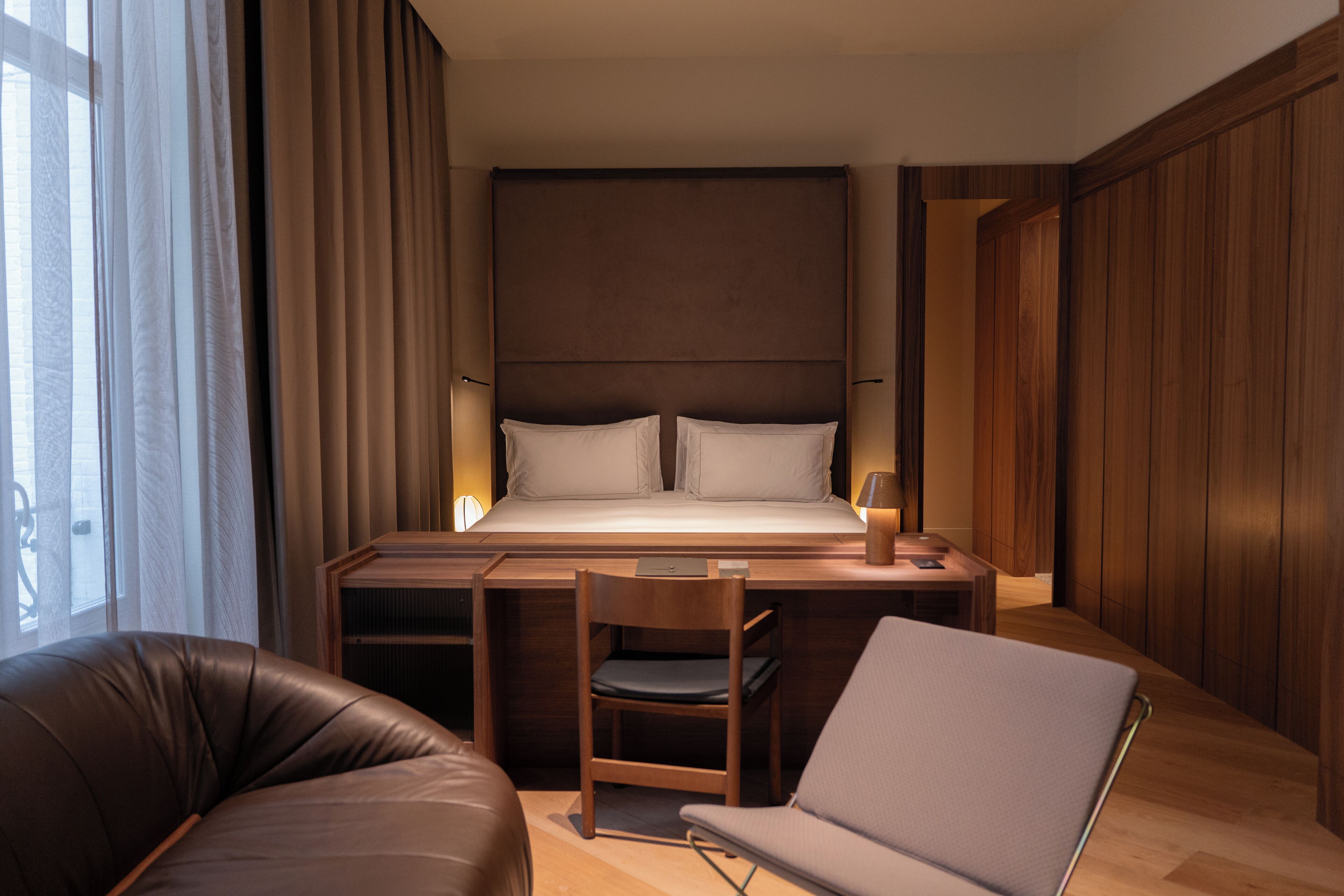 A modern hotel room with a large bed, a desk, a chair, and a laptop.