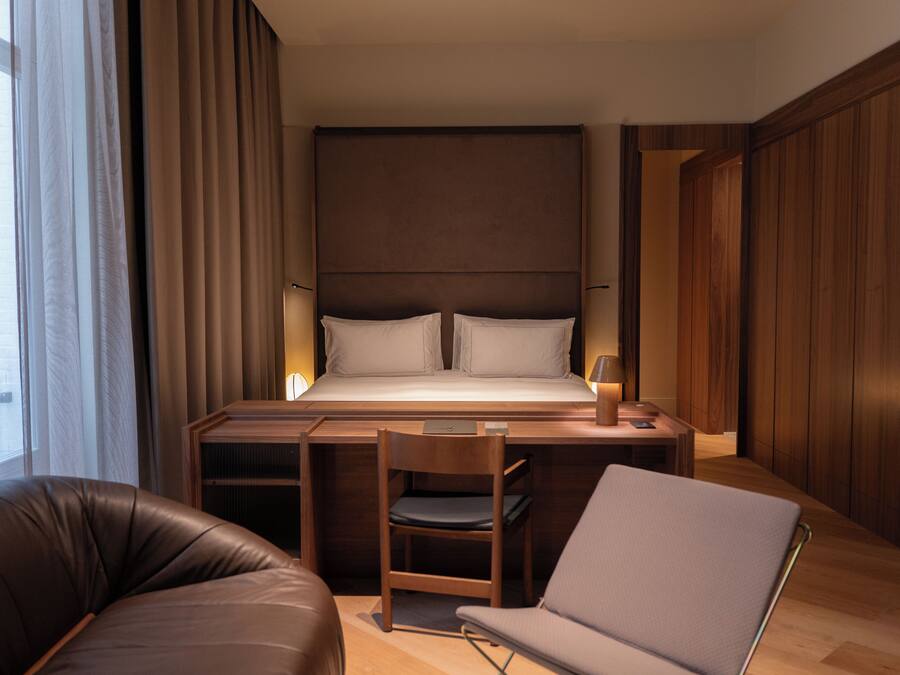 A modern hotel room with a large bed, a desk, a chair, and a laptop.