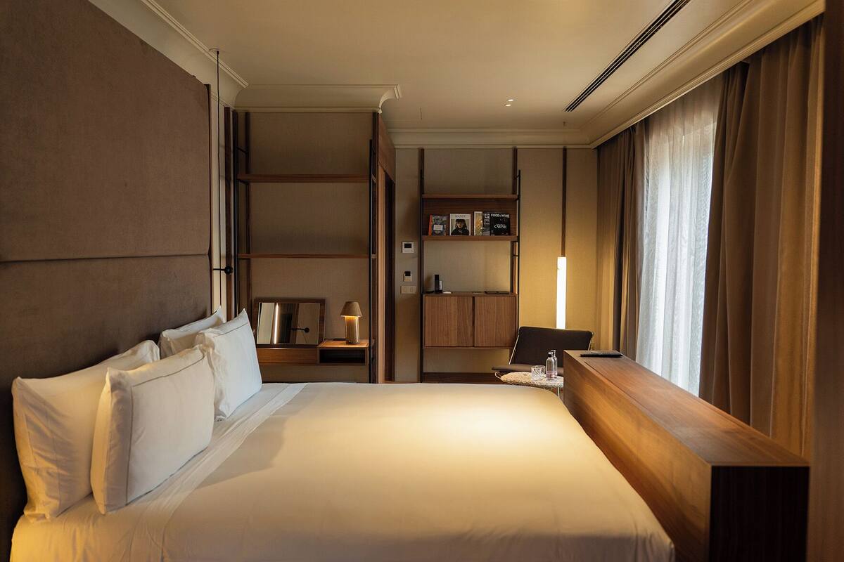 Een hotelkamer met een groot bed, een nachtkastje met een lamp, een kleine tafel met een fles, een stoel en een kledingkast.