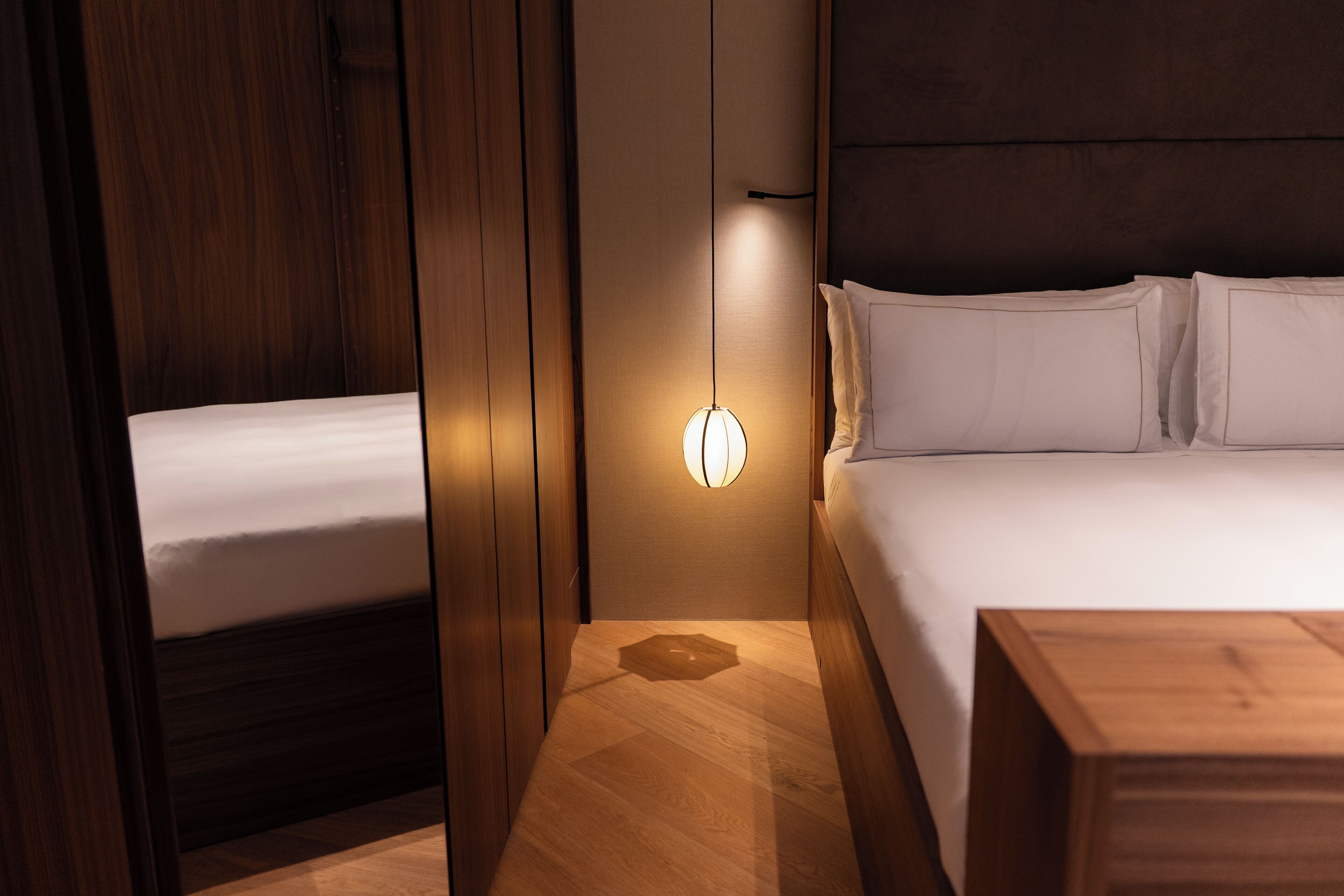 Ein Hotelzimmer mit Bett, Nachttisch, Wandleuchte und Holzboden.