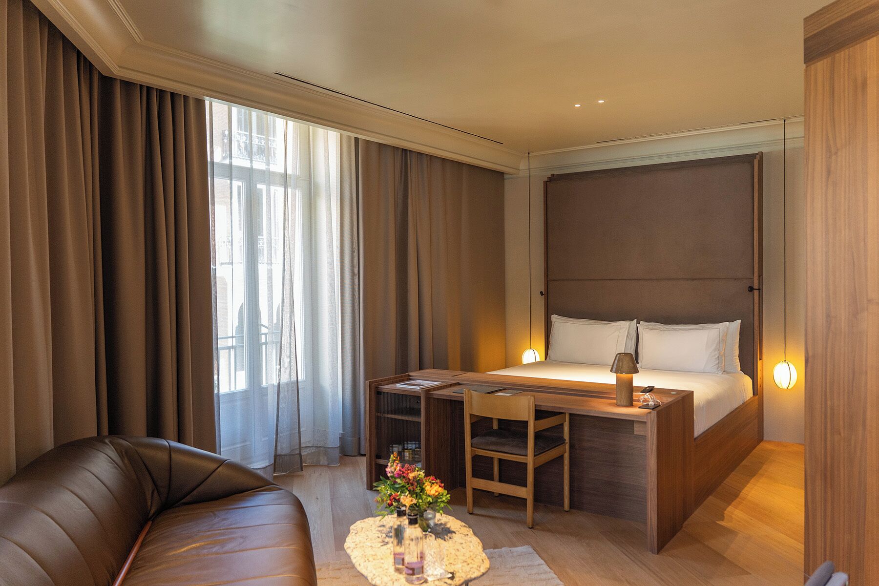 Una habitación de hotel con cama, escritorio, silla, sofá y una pequeña mesa con flores.