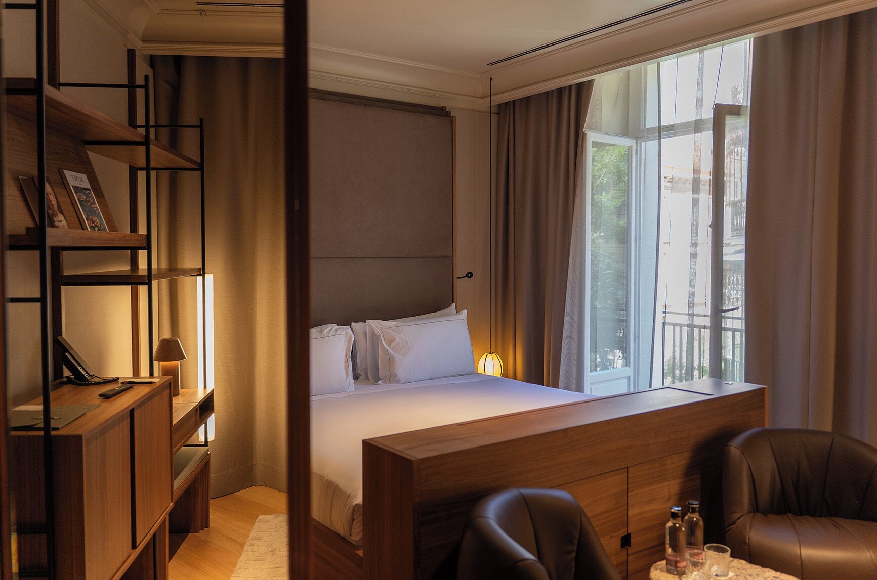 Habitación de hotel con cama, escritorio, silla y ventana grande con cortinas.
