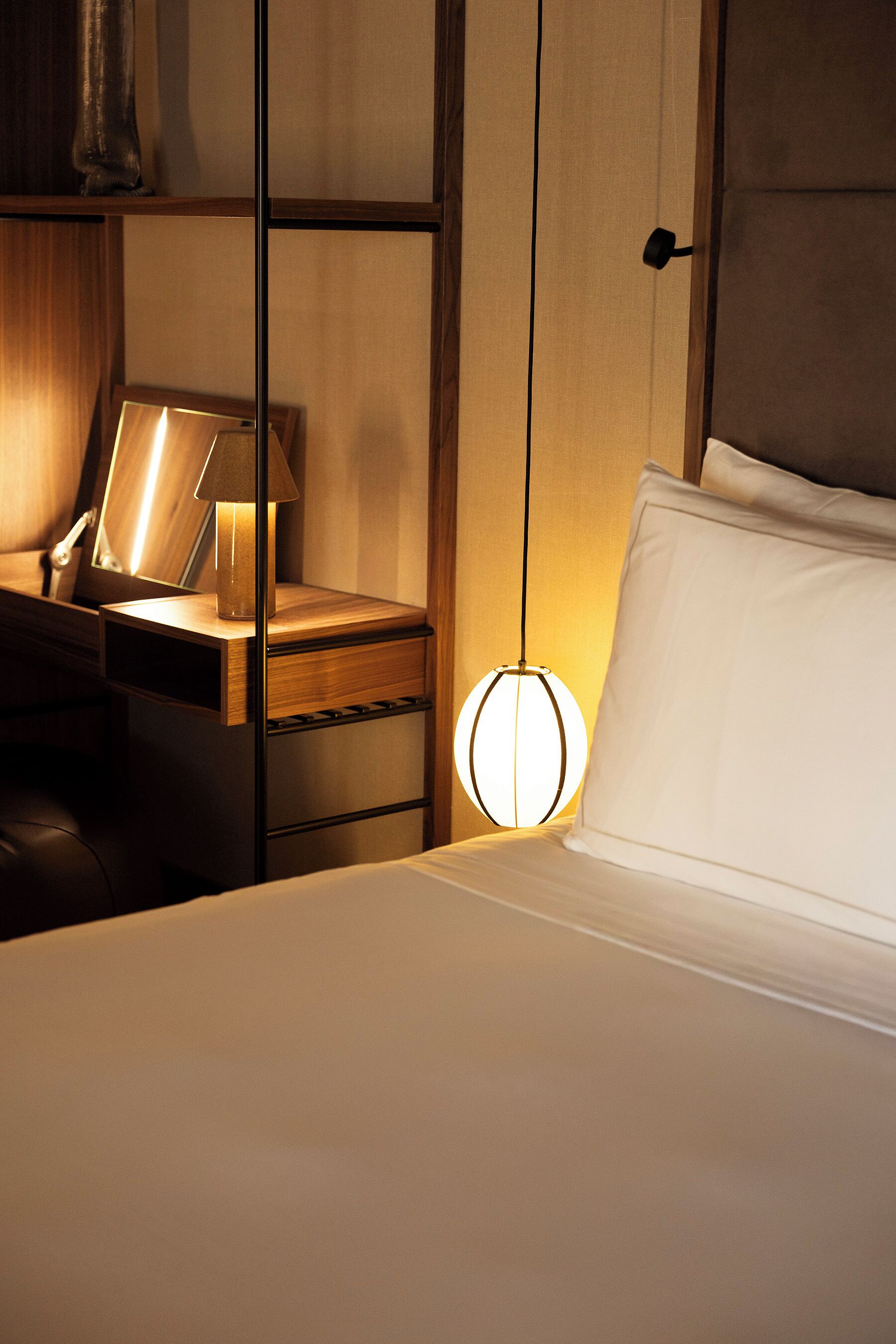 A hotel room with a bed, bedside table, lamp, and a wall-mounted shelf.