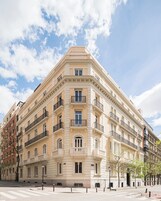 A multi-story building with a classical architectural style, featuring balconies, large windows, and a corner location.