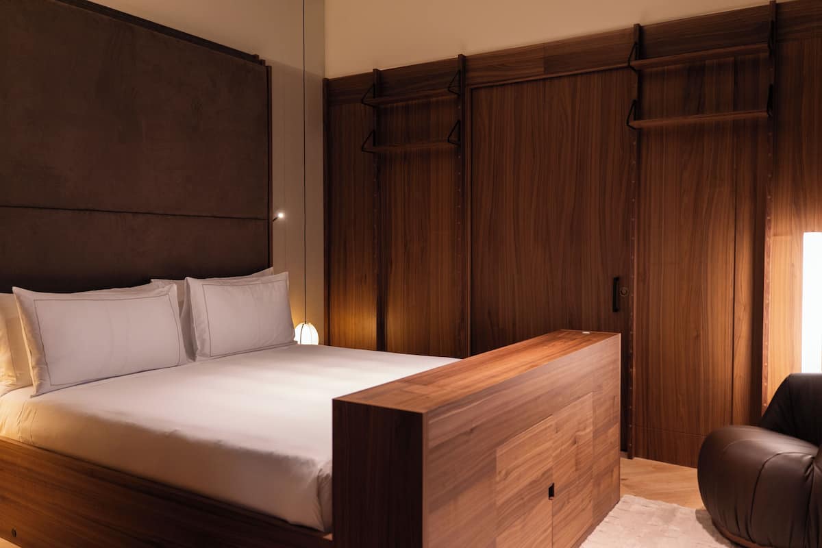 Een slaapkamer met een groot bed, een houten garderobe en een zithoek.
