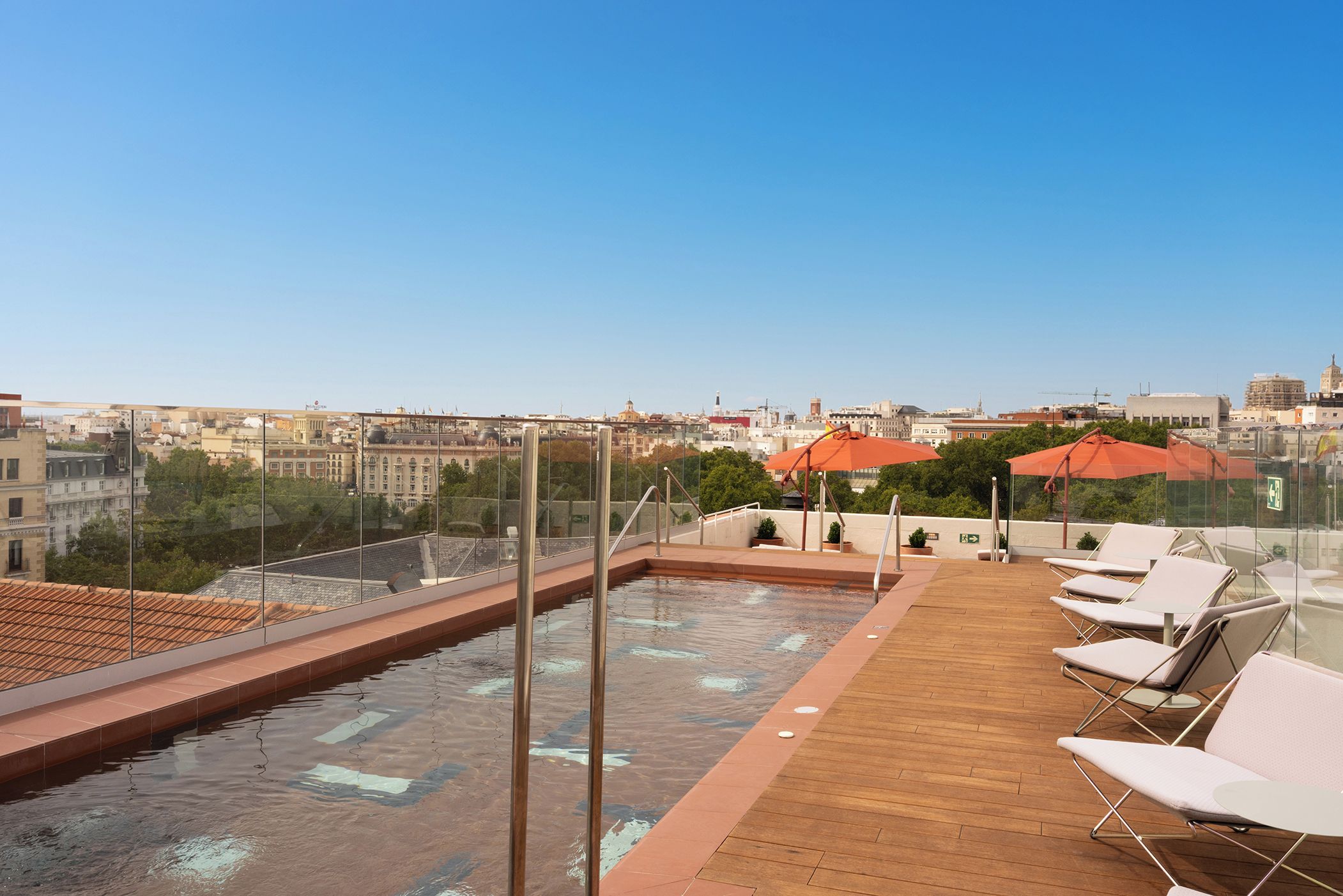 Área de piscina no terraço com espreguiçadeiras e vista para a paisagem urbana.