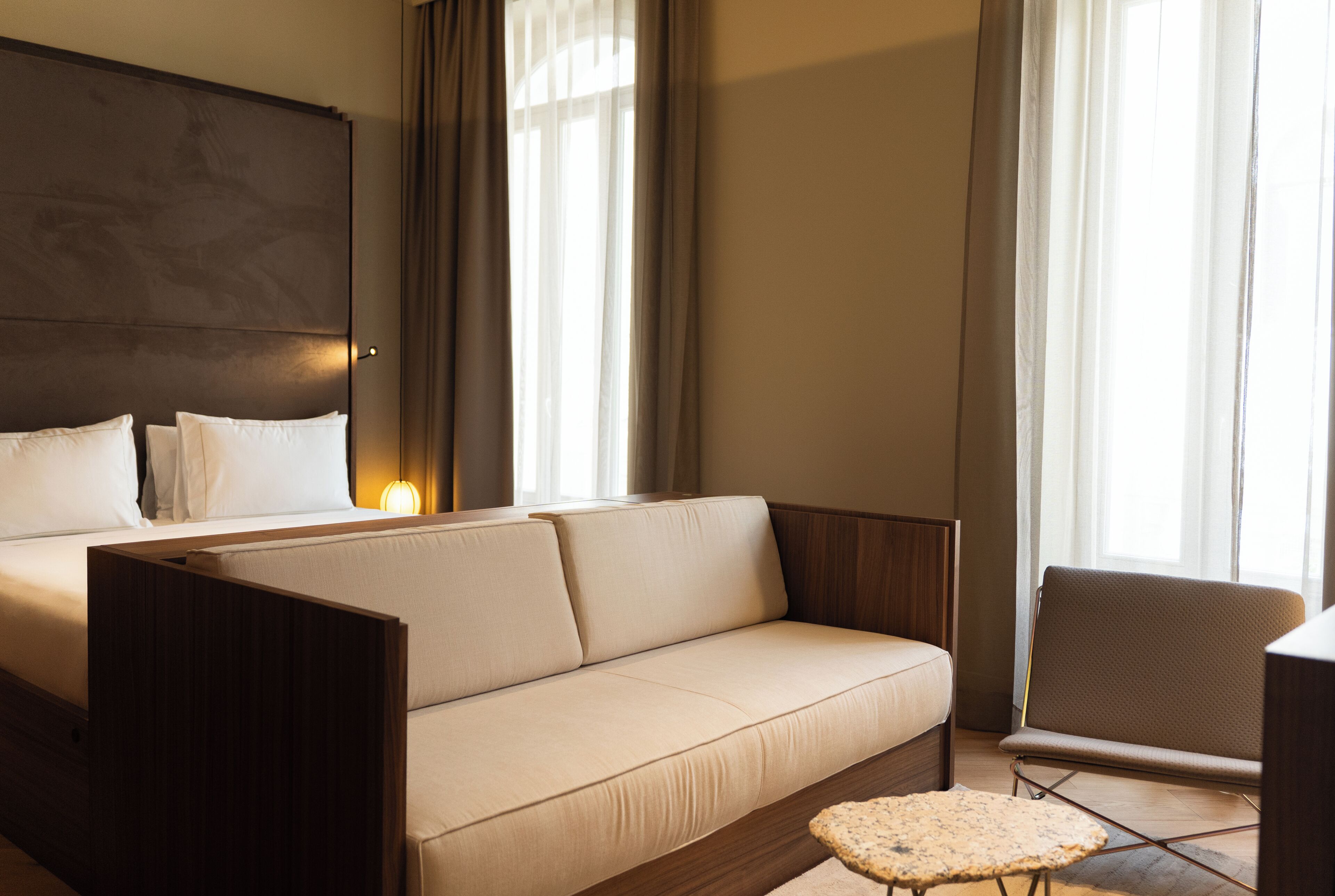 A modern hotel room with a large bed, a sofa, a small table, and a chair.