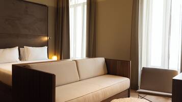 A modern hotel room with a large bed, a sofa, a small table, and a chair.