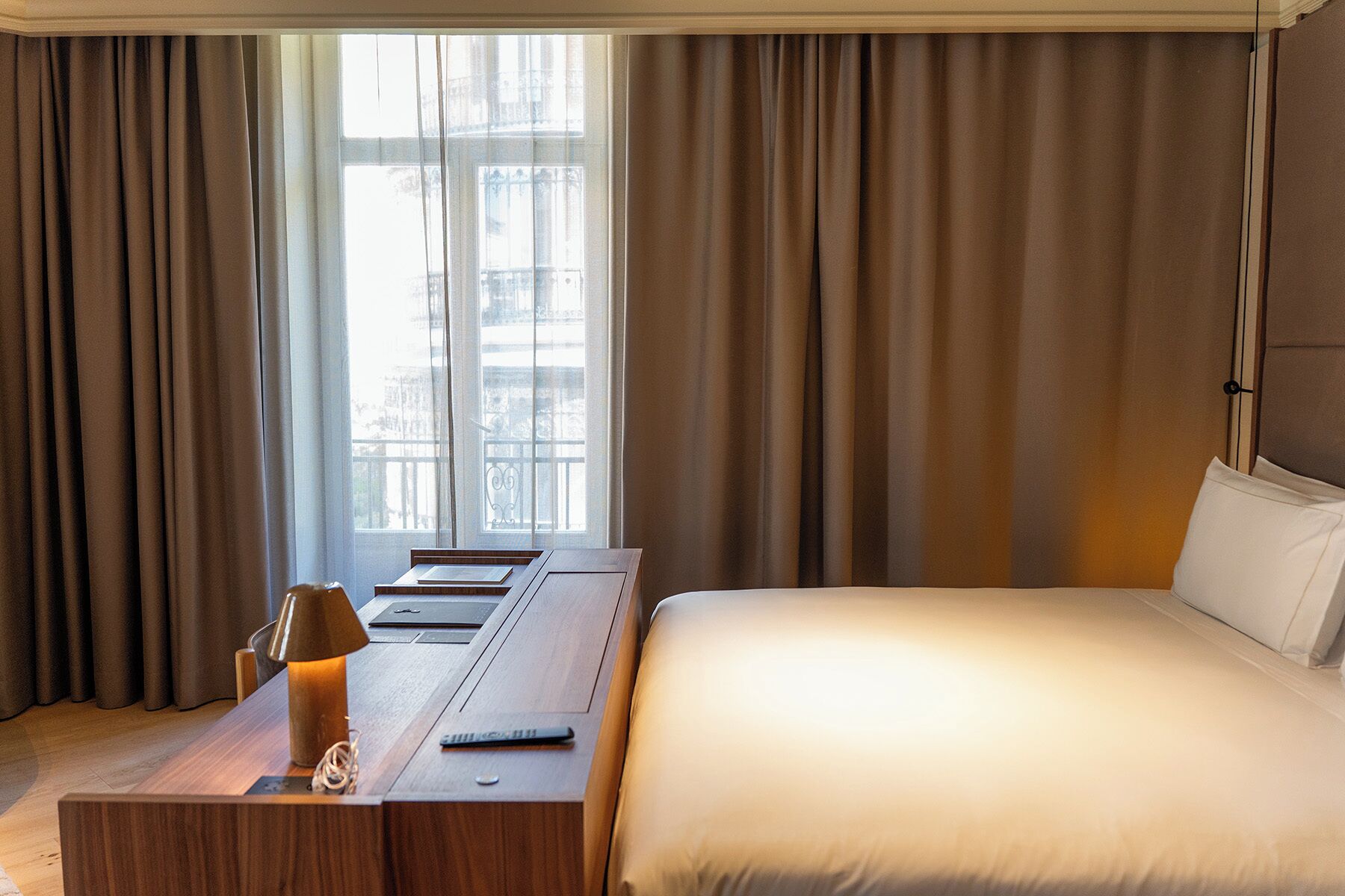 Una habitación de hotel con cama, escritorio con lámpara y ventana con cortinas.