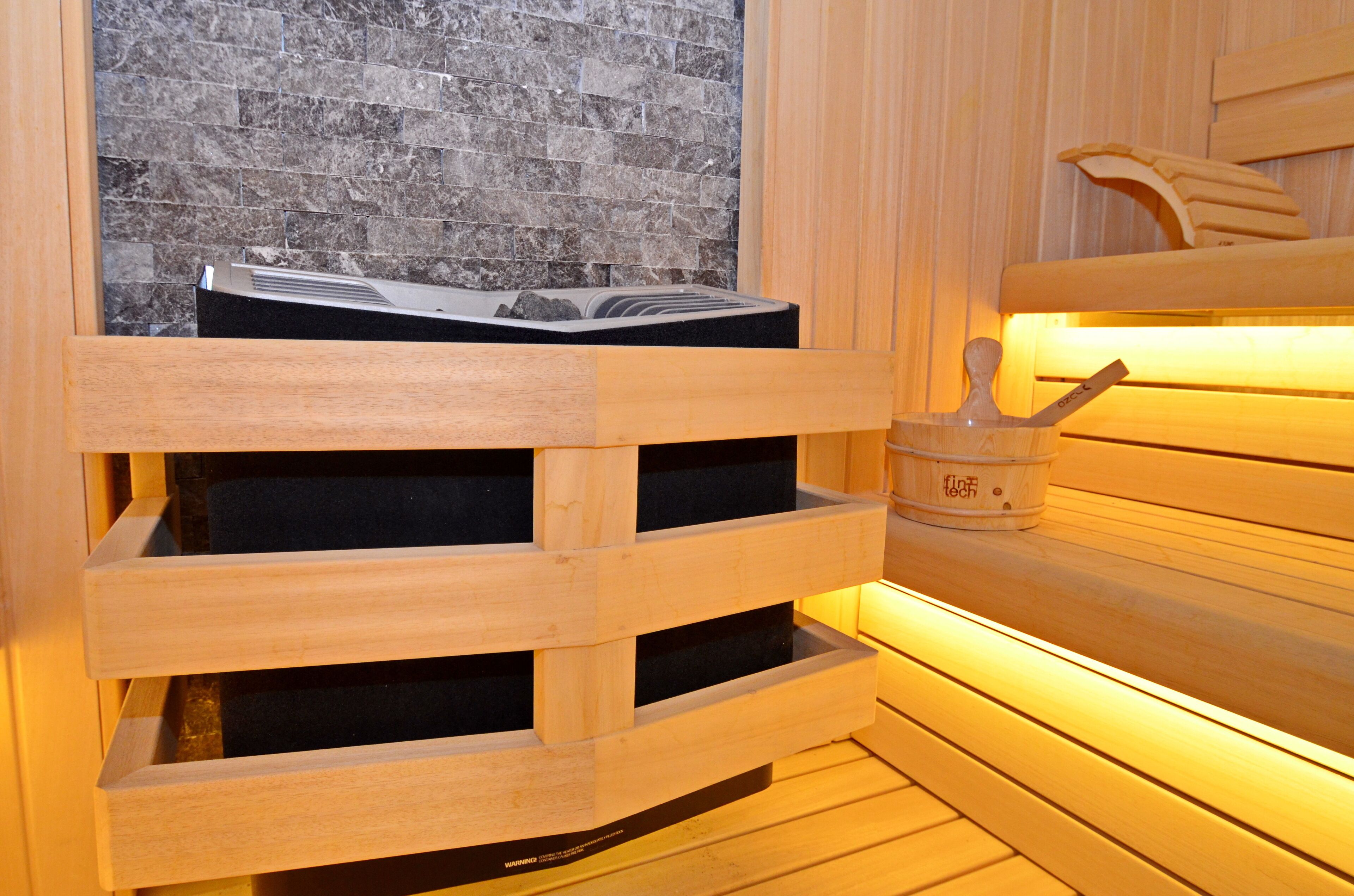 Una sauna de madera con un fondo de pared de piedra y un banco de madera.