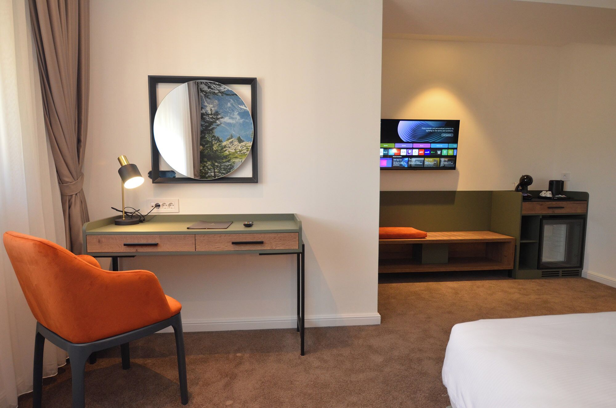 A hotel room with a desk, a chair, a bed, a TV, and a window with curtains.