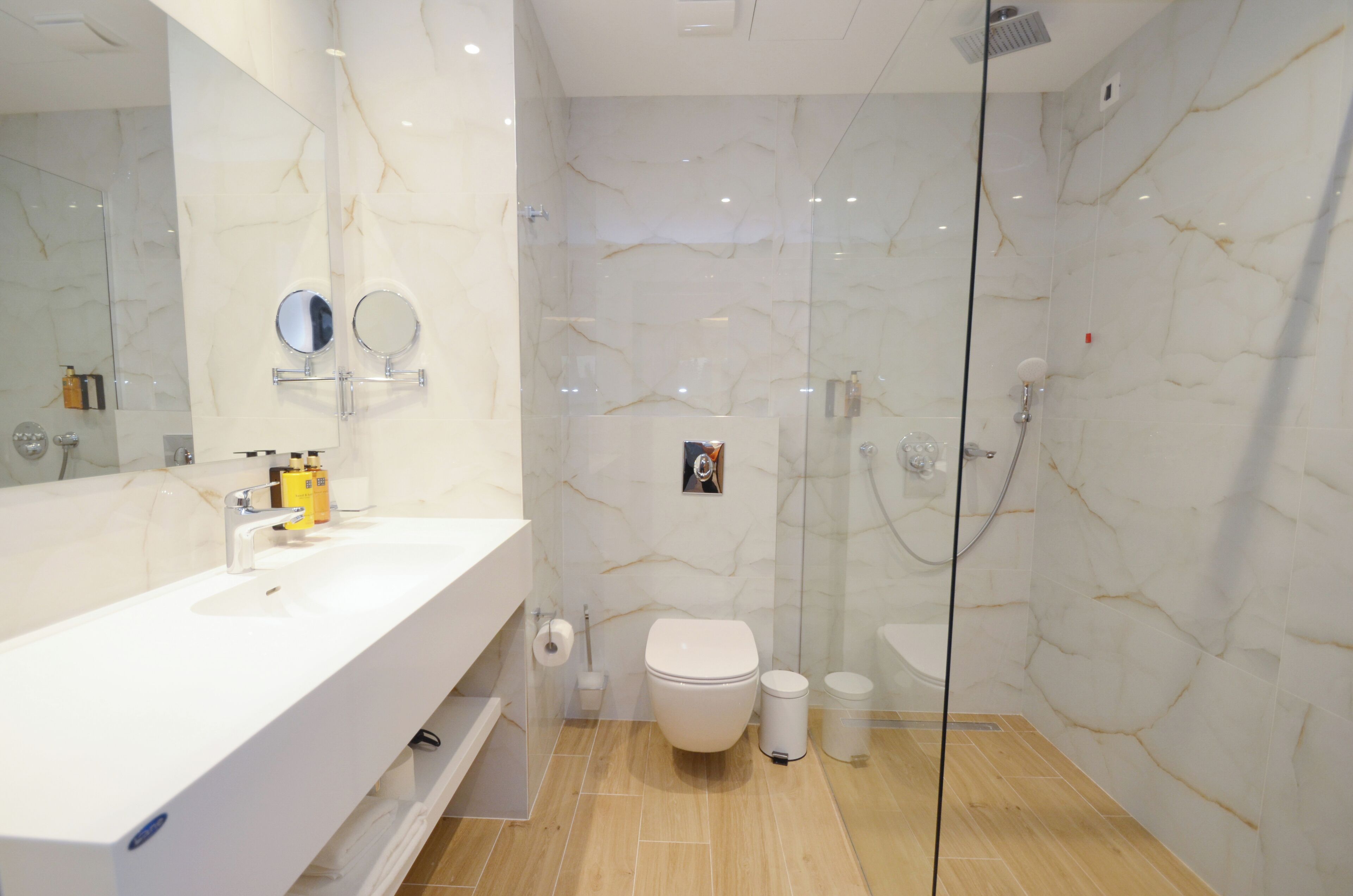 Un bagno moderno con parete in marmo, box doccia in vetro, lavandino bianco e water.