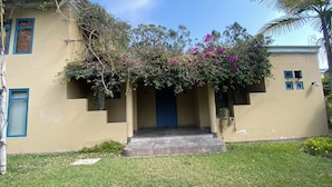 Un bâtiment avec une porte bleue, un petit porche orné de plantes grimpantes et une pelouse verdoyante.