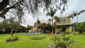 Une pelouse bien entretenue, agrémentée d’une piscine, de palmiers et d’un bâtiment à la façade jaune.