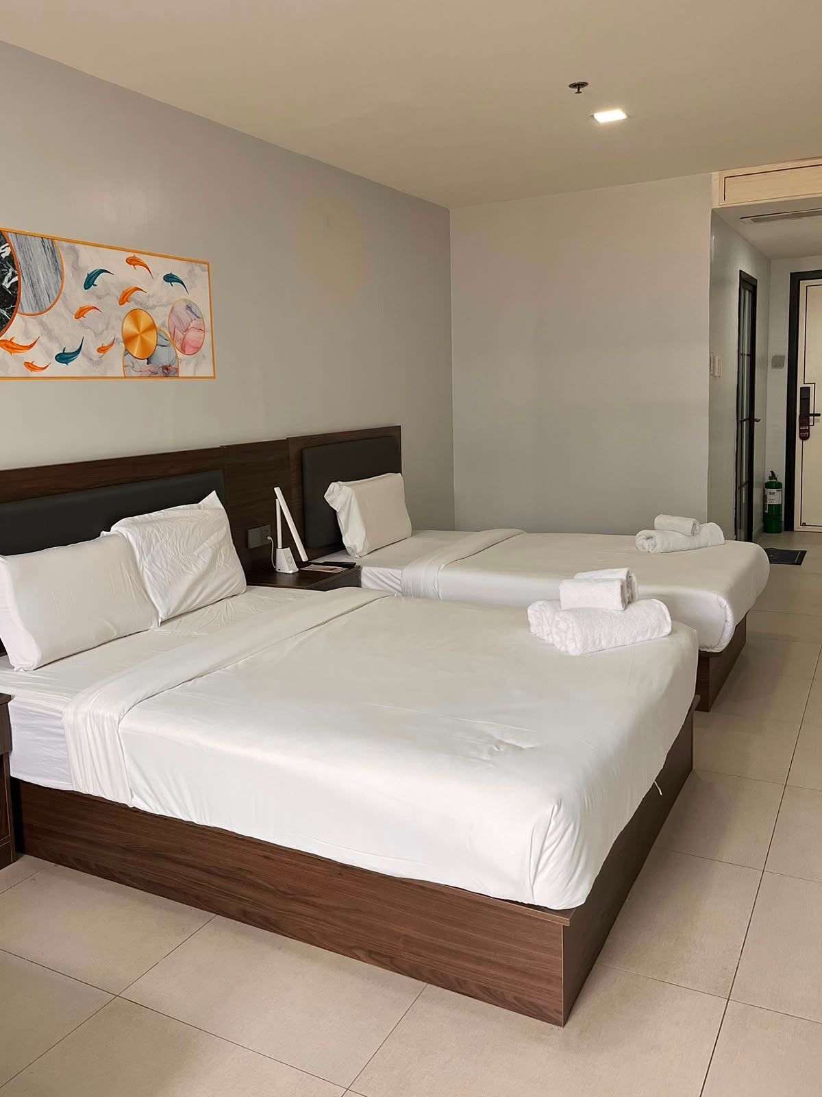 A hotel room with two beds, a painting on the wall, and a door leading to another room.