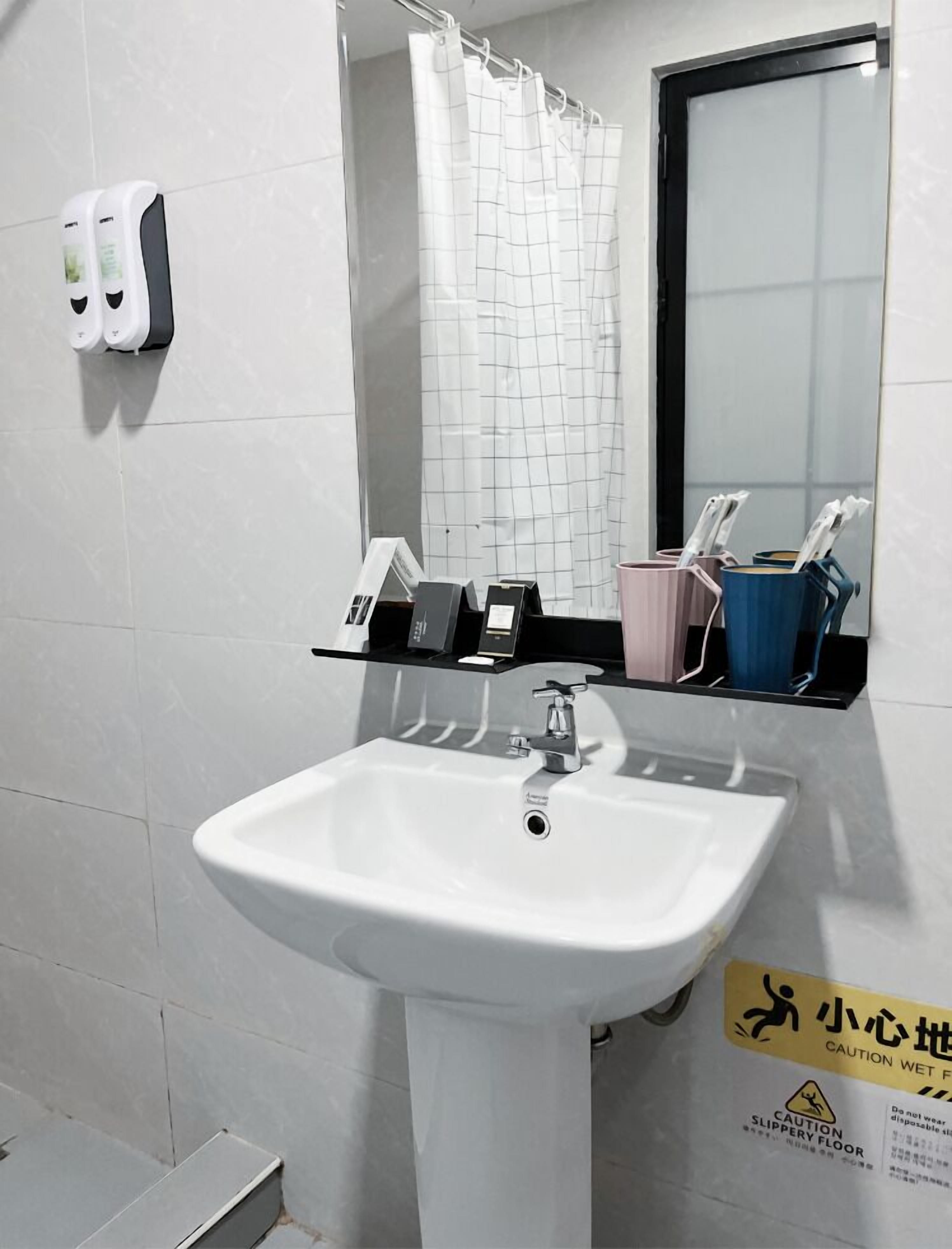 A bathroom with a white sink, a mirror, a shower curtain, and a caution sign on the floor.