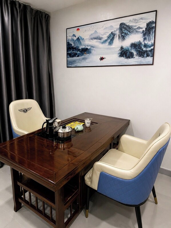 A dining area with a wooden table, two chairs, a painting of a mountainous landscape, and a curtain. - LUNA HOTEL (Pasay)