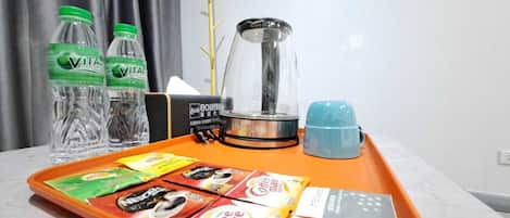 Habitación de hotel con una bandeja que contiene botellas de agua, una cafetera y sobres de café.