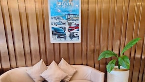 A reception area with a sofa, a potted plant, a table with brochures, and a poster advertising private car service.