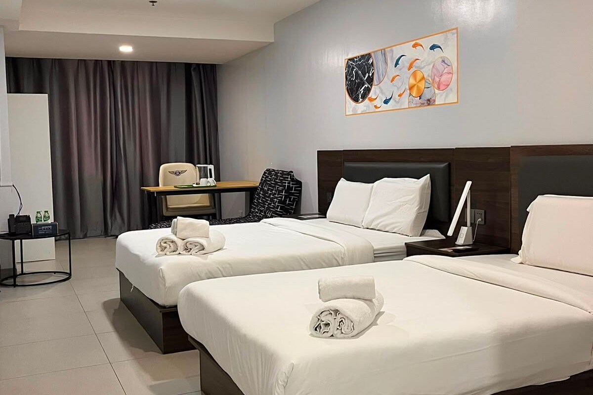 A hotel room with two beds, a desk, and a wall-mounted artwork.