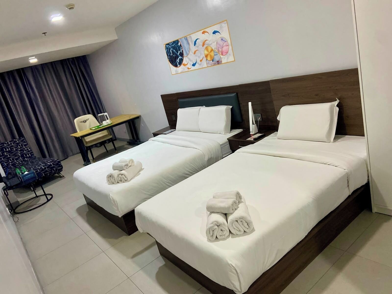 A hotel room with two beds, a desk, a chair, and a painting on the wall.