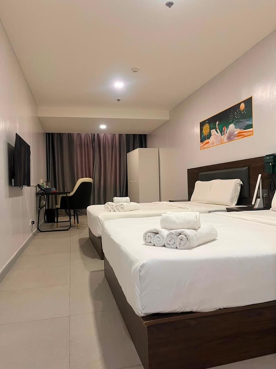 A hotel room with two beds, a desk, a chair, a TV, and a painting on the wall.