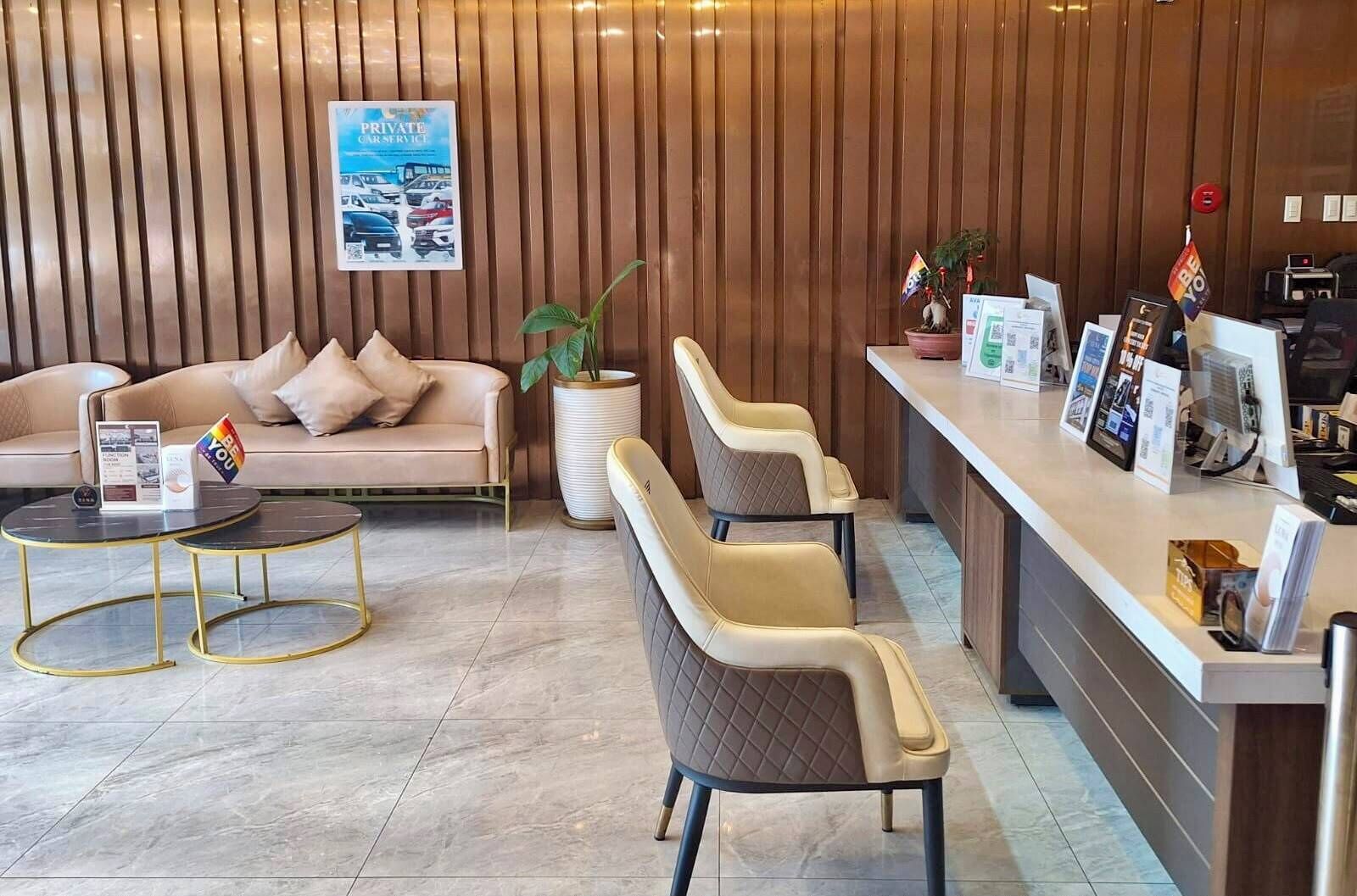 Un espace d’accueil comprenant un canapé, des fauteuils, un comptoir de réception, une plante et un panneau d’affichage.