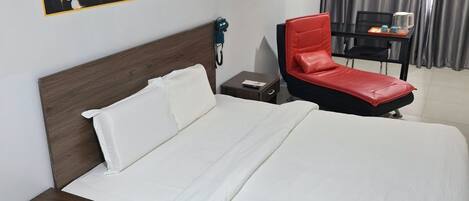 A hotel room with a large bed, a red chair, a small table with a kettle, and a painting on the wall.