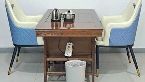A dining area with a table, chairs, a painting, and a trash bin.