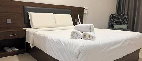Ein Hotelzimmer mit einem großen Bett, einem Nachttisch, einem Hocker, einem fest montierten Telefon und einem Stapel Handtüchern.
