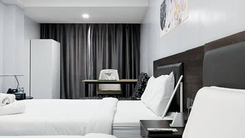 Ett hotellrum med två sängar, ett skrivbord, en stol, en lampa och en tavla på väggen.