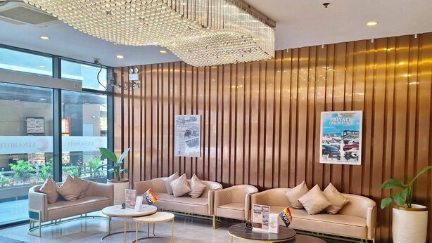 A hotel lobby with a reception desk, two sofas, a chandelier, and a large potted plant.
