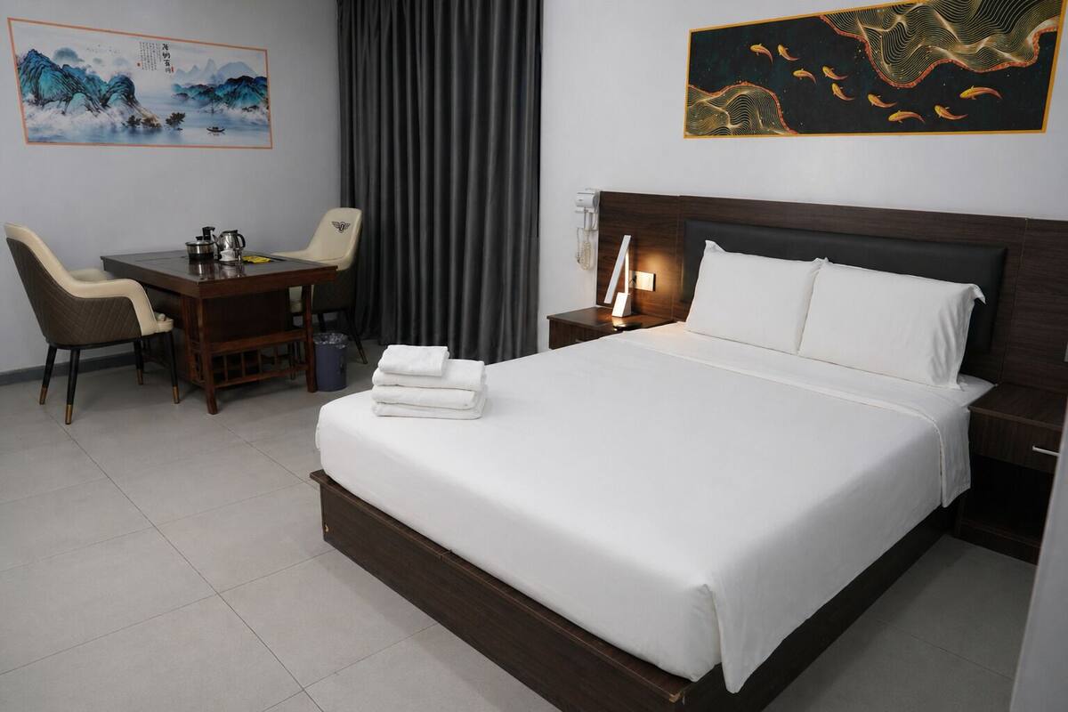 Une chambre d’hôtel comprenant un lit, un bureau avec une chaise, une table avec une chaise, une table de chevet et des œuvres d’art accrochées aux murs.
