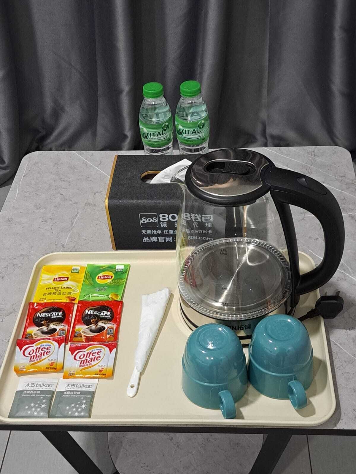 Ein Tisch mit einem Wasserkocher, zwei blauen Tassen, Lipton Teebeuteln, Nescafe Kaffeebeuteln, einer weißen Serviette und zwei Wasserflaschen.