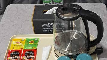 A table with a kettle, two blue cups, Lipton tea packets, Nescafe coffee packets, a white napkin, and two bottles of water.