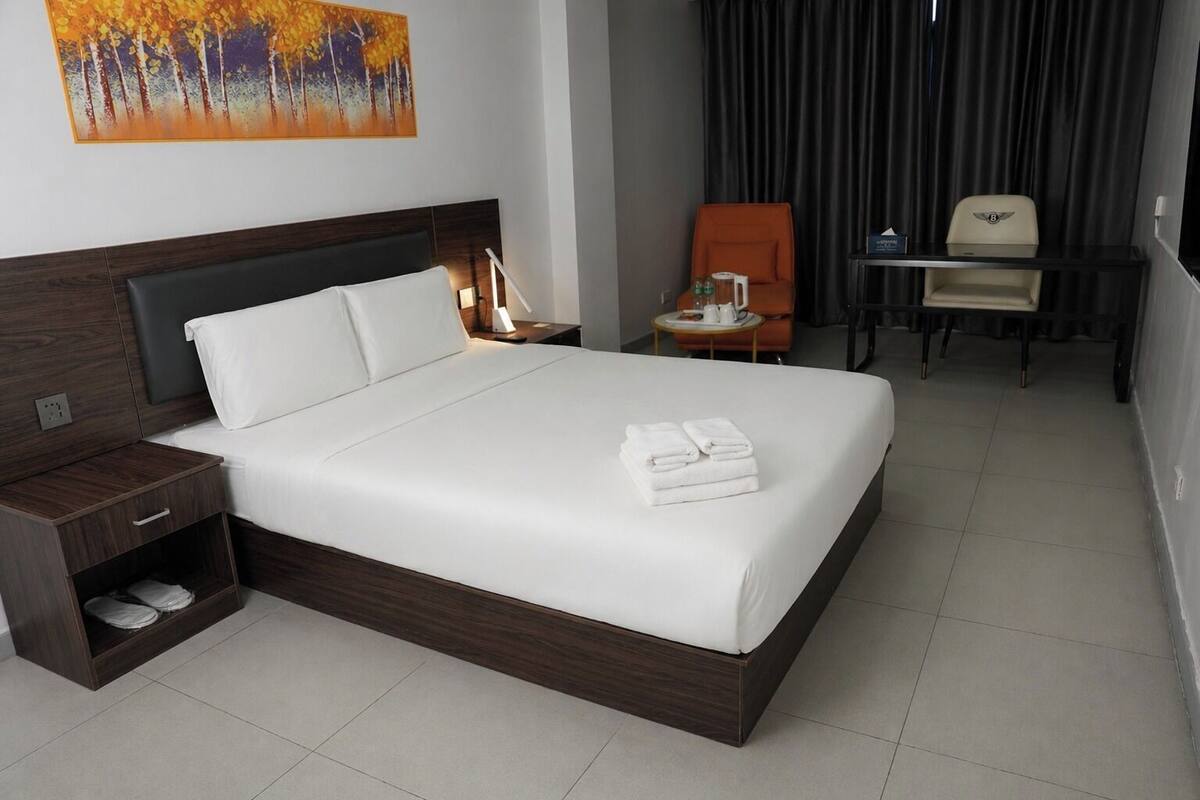 Une chambre d’hôtel avec un grand lit, une table de chevet avec une lampe, une chaise, un bureau avec une autre chaise et un tableau au mur.