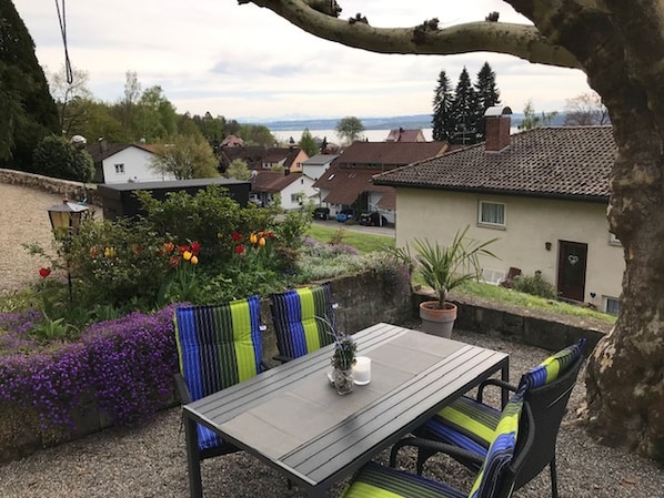 An outdoor patio with a table and chairs, surrounded by a garden with flowers and a view of houses.