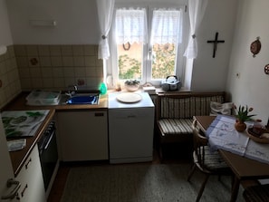 A compact kitchen with a sink, a small refrigerator, a dishwasher, a dining area with a table and chairs, and a window with curtains.